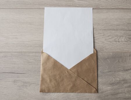 Blank envelope with white blank paper inserted into it on light wood table background. View from above. Mockup for placing your design. Flat lay.の写真素材