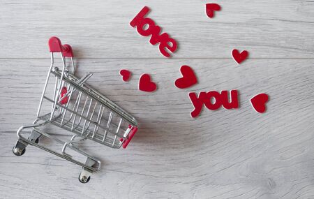 Shopping cart and love inscription inside with red hearts on a wood background. Top view