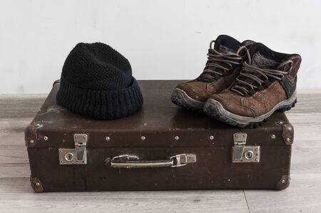 Retro suitcase with male shoes and winter hat on wooden floorの写真素材