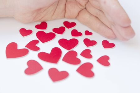 Women's hands hold many red hearts in the palm against the white background. Concept of saving love