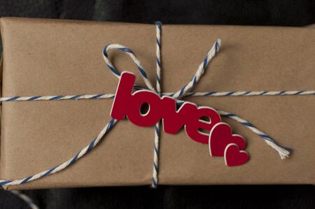 Handcrafted gift box wrapped in kraft paper with red heart, rope and Word LOVE. Top view, flat lay