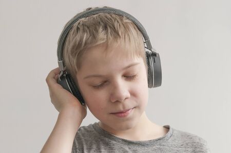 Stylish teen boy listening music in headphones and singing against white background. School child listening loud music in wireless earphonesの写真素材