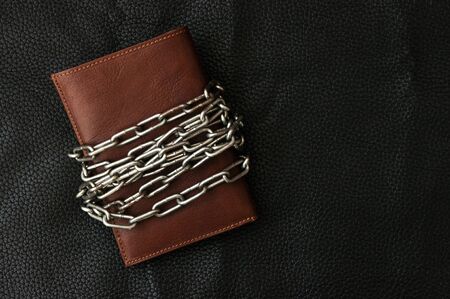 Brown leather wallet bound by an old metal chain in a conceptual image of monetary security or controlling spendingの写真素材