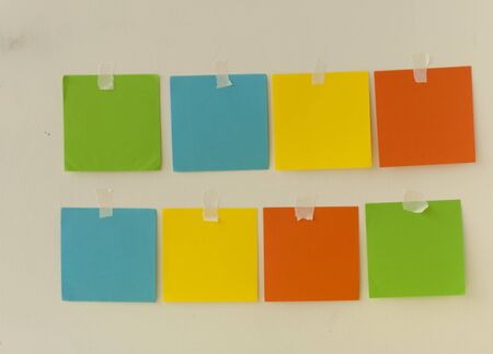 lot of blank square paper colorful stickers on a white wall, close up