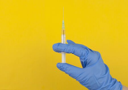 A hand in a blue glove holds a syringe. Medical background. The doctor holds a syringe for...