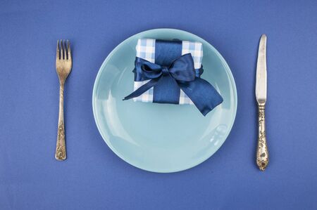 ceramic plate with a cutlery and gift box on the blue paper background. Concept Father's Day or Birthday background. Top view. International men's day concept.の写真素材