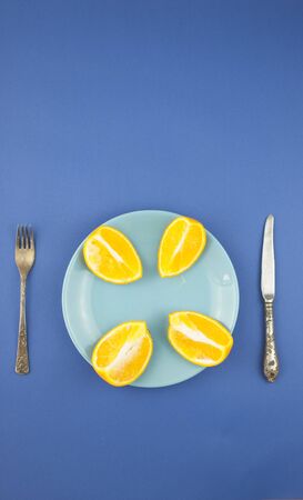 four slices of juicy orange on top on a ceramic plate, knife and fork. On a blue paper background. The view from the topの写真素材