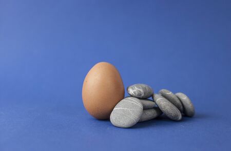 Egg with stack of sea stones on blue background. Easter holidays concept. Copyspace, place for text...