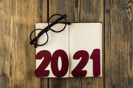 Copy space of number 2021 lay on open vintage book and eyeglasses on wood table background with text...
