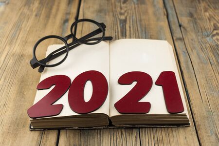 Copy space of number 2021 lay on open vintage book and eyeglasses on wood table background with text...