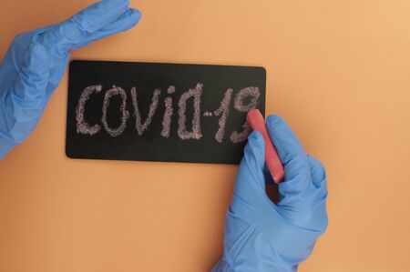 woman hands in blue medical glove hold Covid-19 word written on a small blackboard. Protection...