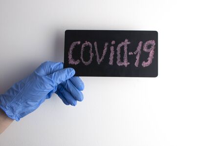 woman hands in blue medical glove hold Covid-19 word written on a small blackboard. Protection conceptの写真素材