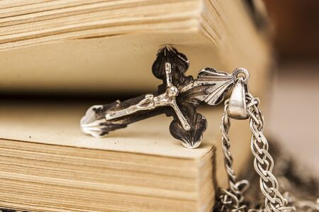 Closeup of Christian cross with silver chain on blank open book with a wooden background