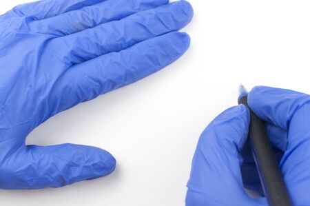 A female hand in a medical glove holds a pen and writes in the air on a white background. Copyspace....