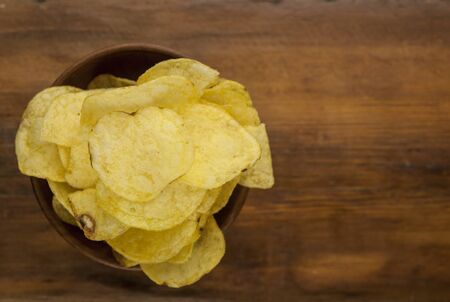 yellow chips from natural potato in brown bowl on wooden background, top view, close-up の写真素材