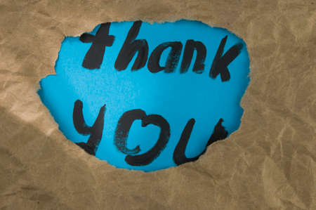 The text THANK YOU behind torn brown paperの写真素材