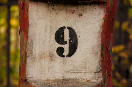The numeral or number nine 9, a black-painted number engraved into to a wooden plank.