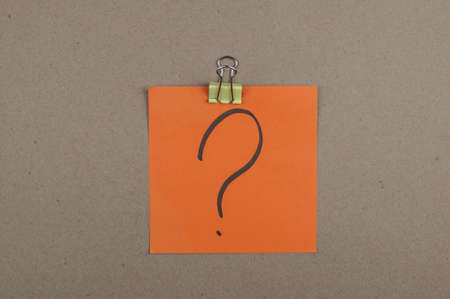 Orange paper note with question mark on brown board. Close up.