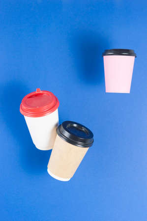 disposable paper flying coffee cups on a blue background hanging on. Takeaway coffee concept....