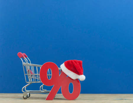 Christmas big sales: shopping cart with Santa hat and symbol of percent on wooden backgroundの写真素材