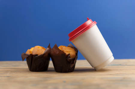 Classic banana nut muffins in black paper wrapper with disposable paper coffee cups on wooden table.