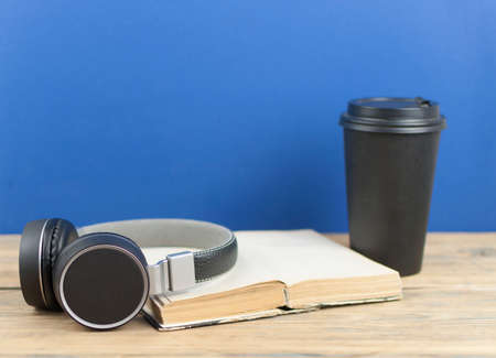 Black paper coffee cup, headphone, old book on wood table with beautiful dark blue backgroundの写真素材