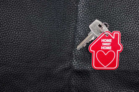 Silver key house with house shaped keychain on black leather background. Real estate concept for...