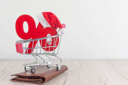 Shopping cart from the supermarket and sign percent with Santa hat on white background. Shopping in...