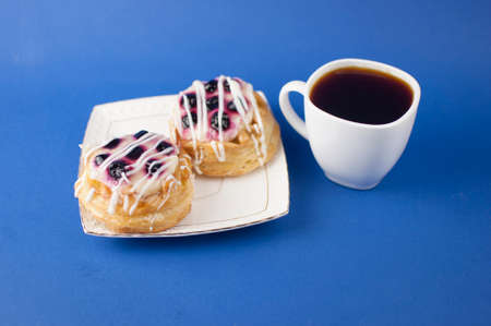 Cup of hot coffee and sweet pastries on blue background