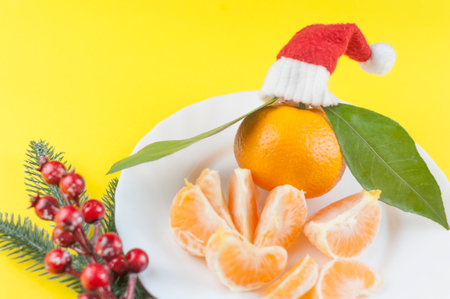 Fresh oranges bowl and green leaf with red Santa hat on yellow backgroundの写真素材