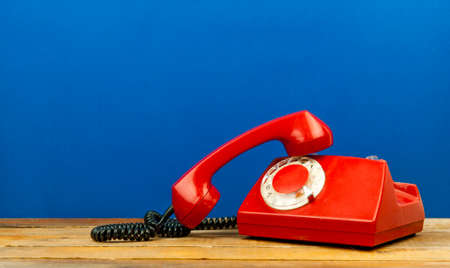 Retro rotary telephone on wooden table over blue wall in roomの写真素材