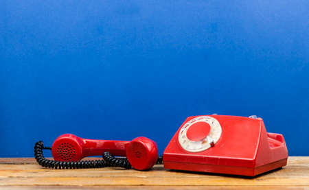 Retro rotary telephone on wooden table over blue wall in roomの写真素材