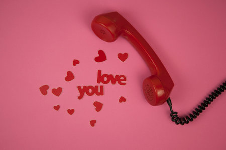 Old telephone handset and red heart on pink paper background. Valentine day.