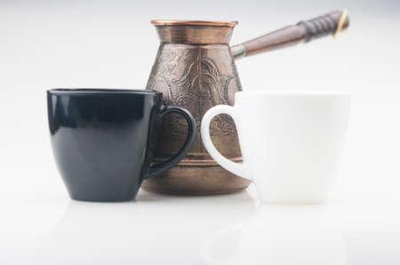 Black and white cups of coffee, copper cezve on white backgroun. Low key. Copy spaceの写真素材