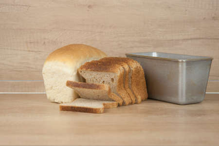 Homemade toasted whole wheat bread and metal form for bread on wood table