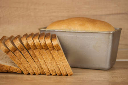 Homemade toasted whole wheat bread and metal form for bread on wood table
