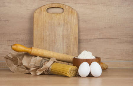 Spaghetti pasta in paper bag with eggs, flour and rolling pin on wooden table
