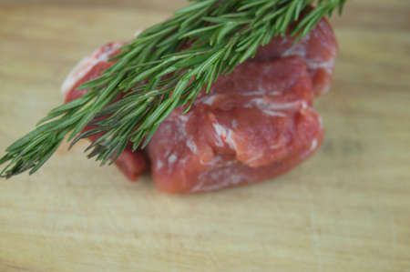 A large piece of pork and two sprigs of rosemary on a wooden table. Ingredients for cooking meat dishes.の写真素材