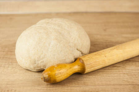 Dough for pizza and rolling-pin on wooden table