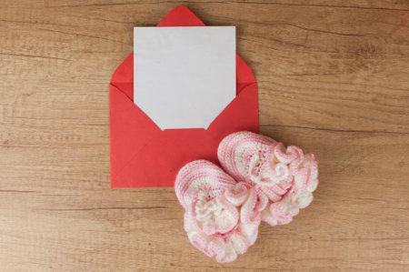 colorful handmade knitting baby shoes and envelope with blank paper sheet on wood table top. Place for text or congratulationsの写真素材