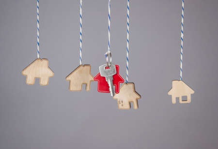 Miniature houses with silver key hanging by strings against gray paper background. Real estate, insurance concept, mortgage, buy sell house, realtor conceptの写真素材
