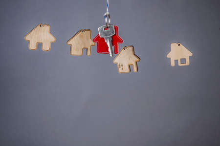 Miniature houses with silver key hanging by strings against gray paper background. Real estate, insurance concept, mortgage, buy sell house, realtor conceptの写真素材