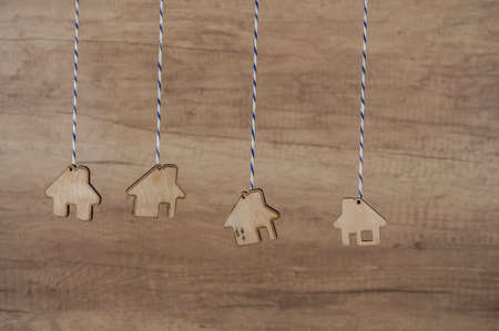Miniature houses hanging by strings against wooden wall background. Real estate, insurance concept, mortgage, buy sell house, realtor conceptの写真素材