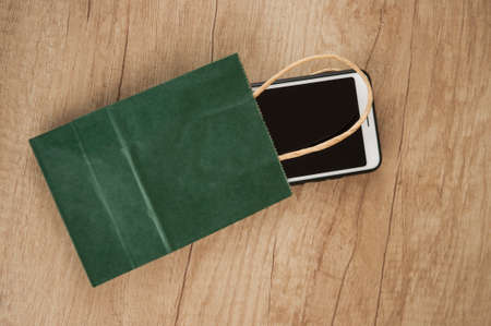 Sale concept - green shopping bag and white smartphone on wood tableの写真素材