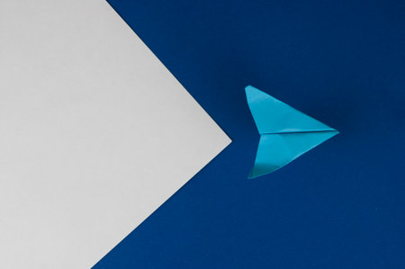 A plane made of paper on a blue background. The plane is made by hand. Origami paper. The idea of...
