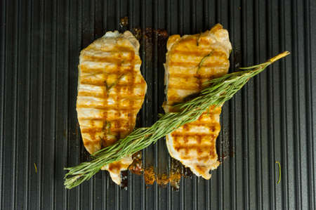 A piece of fresh meat with coarse salt and a sprig of rosemary. Juicy pork steak on the electric...
