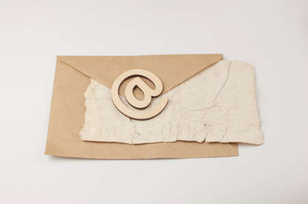 An e-mail sign on a brown envelope with blank crumpled old paper sheet lies on a white background. Concept e-mail message letterの写真素材