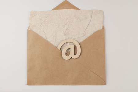An e-mail sign on a brown envelope with blank crumpled old paper sheet lies on a white background. Concept e-mail message letter. Top viewの写真素材