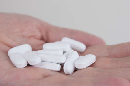 Handful of white round pills in woman palm on a white background. A hand holding heap of small meds....