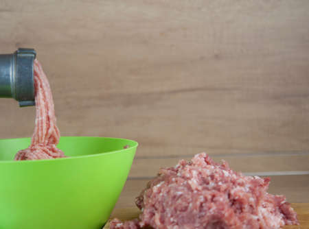 Steel meat grinder processing meat, cooking meat on wooden tableの写真素材